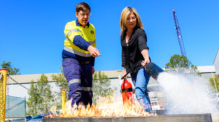 Fire Extinguisher Training showing a woman with a Co2 fire extinguisher putting out a fire while a trainer gives her instruction