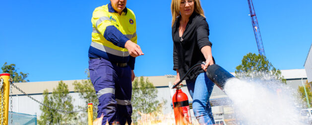 Fire Extinguisher Training showing a woman with a Co2 fire extinguisher putting out a fire while a trainer gives her instruction