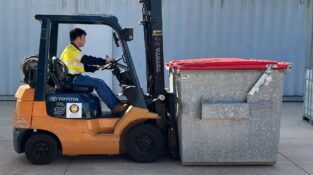 Licence to operate a forklift truck Training showing an orange forklift in a yard lifting a large commercial bin