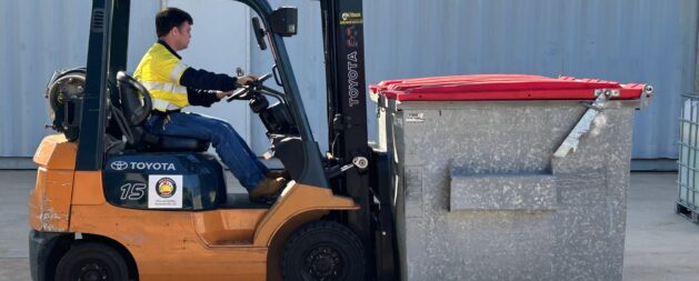 Licence to operate a forklift truck Training showing an orange forklift in a yard lifting a large commercial bin